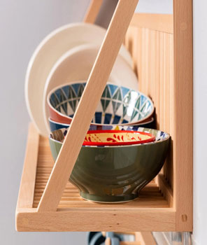 A close up of the side of the plate rack storage shelf showing the find details of the handmade wooden item. In the back ground you can see kitchenware items being stored and displayed. 