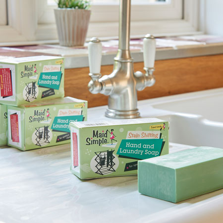 Several packs of our maid simple laundry soap sat one of top of the other, located by a sink. One bar of soap is out of the packaging showing the soap inside.